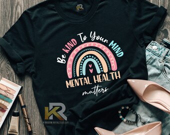May include: Black t-shirt featuring a rainbow design and the text "Be Kind To Your Mind Mental Health Matters".