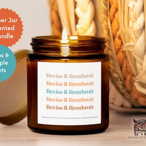 May include: Amber glass jar candle with a white label that reads "Revise & Resubmit" five times. The candle is lit and the flame is visible. The jar is sitting on a wooden surface.