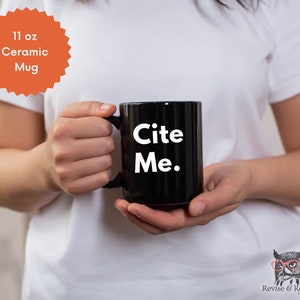May include: A black ceramic mug with the text "Cite Me." in white lettering. The mug is 11 ounces.