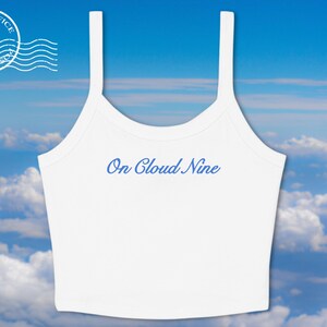May include: White crop top with thin straps and the phrase "On Cloud Nine" in blue script. The top is set against a backdrop of a blue sky with fluffy white clouds. A "Post Office" stamp graphic is in the upper left corner.