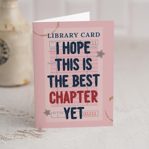 以下が含まれることがあります： 図書館カードのデザインのピンク色のグリーティングカード。「I HOPE THIS IS THE BEST CHAPTER YET」とネイビーブルーと赤のテキストで書かれています。カードは、コーヒーの染みと星のイラストが特徴的なヴィンテージ感があります。