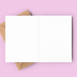 May include: An open, blank white greeting card with a brown envelope on a light pink background. The card is centered, with the envelope partially visible beneath it. Ideal for stationery and paper goods.