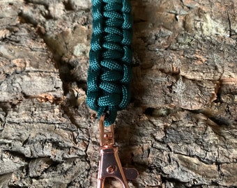 Könnte beinhalten: Ein dunkelgrüner Paracord-Schlüsselanhänger mit einem roségoldenen Metallclip.