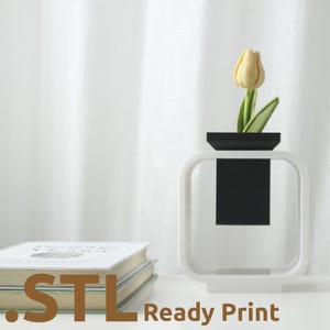 Pode incluir: Um vaso moderno branco e preto com uma tulipa amarela. O vaso tem uma forma quadrada com uma inserção retangular preta. O texto ".STL Ready Print" é visível na parte inferior da imagem.