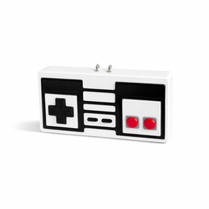 Puede incluir: Un despertador rectangular blanco diseñado para parecerse a un mando de videojuegos clásico. Cuenta con una cruceta negra, botones rectangulares negros y dos botones circulares rojos. El reloj tiene dos perillas plateadas en la parte superior.