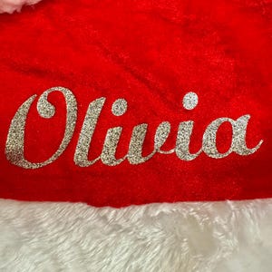 May include: Red and white Santa hat with the name Olivia in silver glitter lettering.