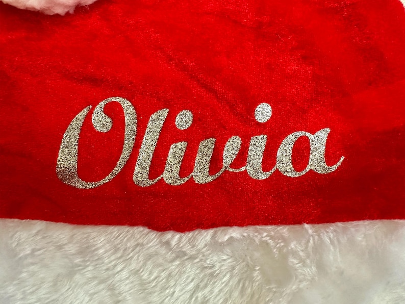 May include: Red and white Santa hat with the name Olivia in silver glitter lettering.