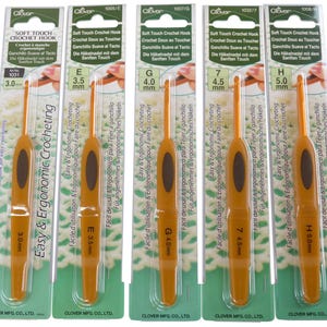 Peut inclure: Ensemble de crochets ergonomiques orange avec des poignées marron, présentés dans leur emballage. L'emballage indique "Soft Touch Crochet Hook" et les mesures en millimètres. Les tailles varient de 2,0 mm à 5,5 mm.