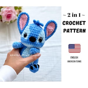 Könnte beinhalten: Eine blau-weiße Stitch-Puppe aus Häkelarbeit mit rosa Innenohren und schwarzen Augen. Die Puppe wird in einer Hand gehalten. Das Bild enthält den Text "~ 2 in 1 ~ CROCHET PATTERN" und die amerikanische Flagge mit "ENGLISH AMERICAN TERMS".