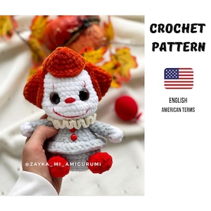 Könnte beinhalten: Gehäkelte Clown-Puppe mit weißem Gesicht, roter Nase und orangefarbenem Haar. Die Puppe trägt ein graues Outfit mit roten Knöpfen und Füßen. Das Bild enthält den Text "CROCHET PATTERN" und eine amerikanische Flagge.