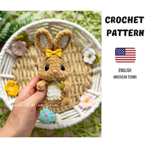 Könnte beinhalten: Ein braun-weißes gehäkeltes Amigurumi-Kaninchen mit einer gelben gepunkteten Schleife, das einen kleinen Gegenstand hält. Der Text CROCHET PATTERN, ein US-Flaggen-Symbol und der Text ENGLISH AMERICAN TERMS sind sichtbar. Das Wasserzeichen ZAYKA_MI_AMIGURUMI ist vorhanden.