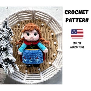 Könnte beinhalten: Gehäkelte Puppe einer Figur mit braunen Haaren, die ein blaues Kleid, einen roten Umhang und schwarze Schuhe trägt. Die Puppe wird in einem geflochtenen Korb mit weißem Makramee-Rand präsentiert. Der Text "CROCHET PATTERN" und "ENGLISH AMERICAN TERMS" sind sichtbar.