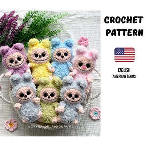 May include: A collection of handmade crochet amigurumi dolls in various pastel colors, including purple, yellow, blue, pink, and green. Each doll has a smiling face and is displayed in a woven basket. The image also includes text that says "CROCHET PATTERN" and "ENGLISH AMERICAN TERMS".