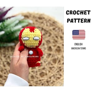 Könnte beinhalten: Gehäkelte Iron Man-Puppe in Rot, Gelb und Weiß. Die Puppe hat einen runden Kopf mit gelbem Gesicht und rotem Helm. Der Text "CROCHET PATTERN" und "ENGLISH AMERICAN TERMS" sind ebenfalls sichtbar.