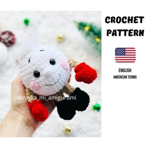 May include: A crocheted white amigurumi doll with black eyes, a smiling face, and pink cheeks. It has red mittens, black shoes, and tan arms. The text "CROCHET PATTERN" and an American flag are visible.