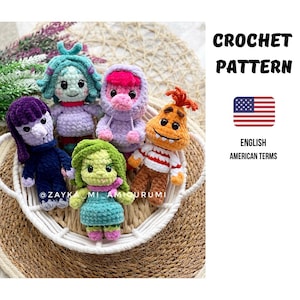 Może przedstawiać: Kolekcja pięciu kolorowych, szydełkowych lalek amigurumi, każda z unikalnymi cechami i wyrazami twarzy. Lalki ułożone są w białym koszu na tkanej powierzchni. Obraz zawiera tekst "CROCHET PATTERN" i "ENGLISH AMERICAN TERMS".