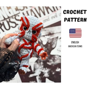 Könnte beinhalten: Handgefertigte Häkelpuppe in Grau-, Rot- und Brauntönen. Die Puppe hat ein einzigartiges Design mit detailliertem Gesicht und Körper. Das Bild enthält auch den Text "CROCHET PATTERN" und eine amerikanische Flagge.