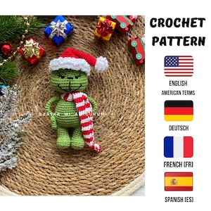 May include: A crocheted green figure resembling the Grinch, wearing a red and white Santa hat and scarf. The image includes Christmas decorations and the text "CROCHET PATTERN". Flags and text indicate English, German, French, and Spanish terms for the pattern.