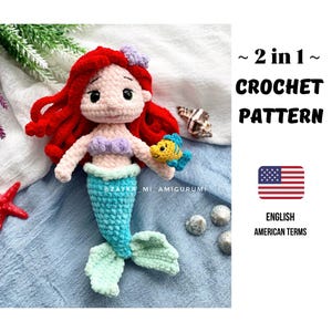 Könnte beinhalten: Eine handgefertigte Häkelpuppe einer Meerjungfrau mit roten Haaren, einem lavendelfarbenen Muscheloberteil und einem türkisfarbenen Schwanz. Die Puppe hält einen gelb-blauen Fisch. Der Text "~ 2 in 1 ~ CROCHET PATTERN" ist enthalten.