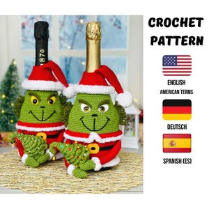 Puede incluir: Dos fundas de botella de ganchillo verdes que se asemejan a un personaje, cada una con un gorro y traje de Papá Noel rojos. Uno sostiene un pequeño árbol de Navidad verde. La imagen incluye el texto "CROCHET PATTERN" y banderas para inglés, alemán y español.