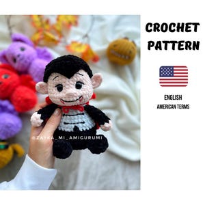 Könnte beinhalten: Gehäkelte Vampirpuppe mit schwarzem Umhang, schwarzem Haar und roter Fliege. Die Puppe hat ein lächelndes Gesicht mit zwei Fangzähnen. Das Bild enthält auch den Text "CROCHET PATTERN" und die amerikanische Flagge.