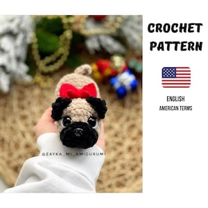 Könnte beinhalten: Ein gehäkelter Mops mit einer roten Schleife. Der Mops hat schwarze Ohren und eine schwarze Schnauze. Das Bild enthält den Text "CROCHET PATTERN" und die amerikanische Flagge mit den Worten "ENGLISH AMERICAN TERMS".