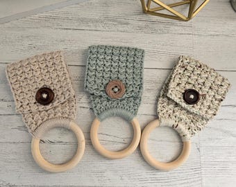 May include: Three handmade crochet towel holders in neutral colors. Each holder features a wooden ring and a crocheted top with a wooden button closure. The colors include beige, sage green, and a speckled cream.