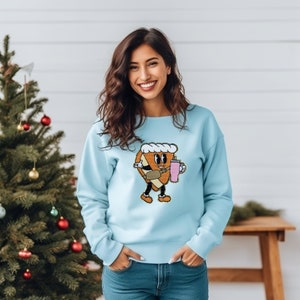 May include: A light blue sweatshirt with a cartoon illustration of a slice of pizza holding a pink drink. The pizza has a smiling face and is wearing a white hat.