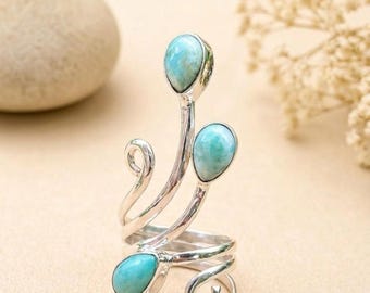 Puede incluir: Un anillo de plata con tres piedras de color azul claro en forma de lágrima engastadas en metal pulido. La banda consta de elementos de alambre de plata curvados y en espiral que se extienden hacia arriba, sosteniendo cada piedra.