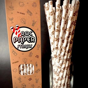 Peut inclure: Une grande boîte rectangulaire en carton étiquetée ROC PAPER STRAWS avec une fenêtre découpée montrant des pailles en papier. La boîte présente des icônes et du texte en ligne brune. Un bocal en verre transparent contient des pailles en papier blanc.