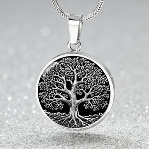 Può includere: Una collana d'argento con un ciondolo rotondo che presenta un design ad albero della vita nero e argento.