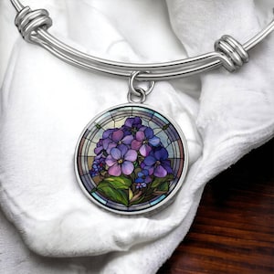 May include: A silver bangle bracelet with a round charm featuring a stained glass design of purple flowers.