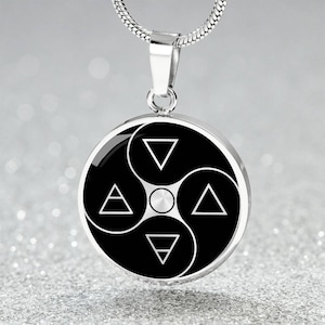 Może przedstawiać: Srebrny naszyjnik z wisiorkiem. Okrągły wisiorek ma czarno-biały wzór z czterema białymi trójkątami i centralnym okręgiem, w stylu yin-yang. Łańcuszek naszyjnika to srebrny łańcuszek typu snake.