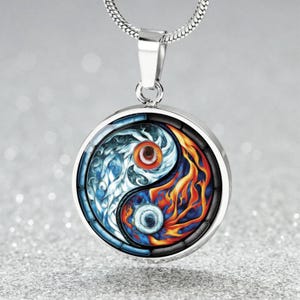Könnte beinhalten: Eine silberfarbene Halskette mit Anhänger, die einen runden Anhänger mit einem Yin-und-Yang-Design zeigt. Das Design ist in zwei Hälften geteilt: eine Seite zeigt Wasser in Blautönen, die andere Feuer in Orange- und Rottönen.