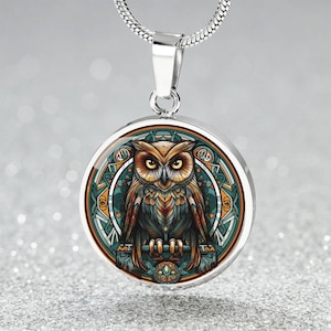 May include: A silver necklace with a round pendant featuring a colorful owl illustration with intricate details. The owl is surrounded by a circular design with geometric patterns in shades of blue, green, and orange.