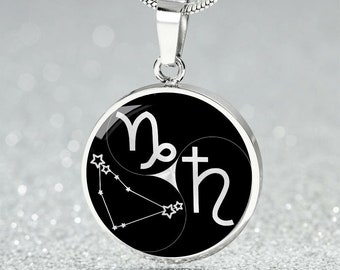 Può includere: Collana con pendente argentato con pendente rotondo. Il pendente ha uno sfondo nero con simboli e dettagli della costellazione del Capricorno bianchi. La collana ha una catena d'argento.