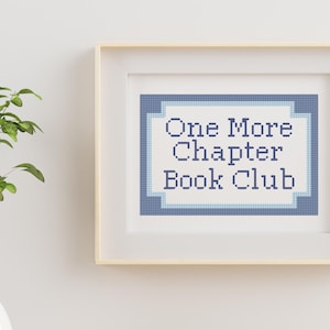 Peut inclure: Une broderie au point de croix encadrée présentant le texte One More Chapter Book Club en lettres pixelisées bleu foncé. Le motif est centré sur un fond blanc avec une bordure géométrique bleue et bleu clair dans un cadre en bois clair.