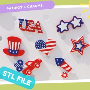 May include: A collection of seven patriotic charms featuring red, white, and blue designs including the text USA, star-shaped glasses, a top hat, a heart with stars and stripes, a star, a red car, and a firework. The charms are displayed on a white board.