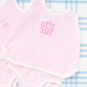 Peut inclure: Deux chemises roses sans manches avec des bordures blanches. Une chemise a le nom "Camille" brodé sur le devant avec des nœuds. L'autre chemise a un monogramme brodé sur le devant.