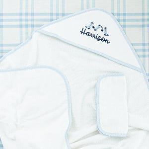 May include: White hooded towel with blue trim and a blue embroidered design of cowboy boots and stars. The towel is personalized with the name "Harrison".