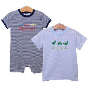 Könnte beinhalten: Zwei gestreifte Babyshirts mit gestickten Namen. Das blaue Shirt hat ein Auto- und LKW-Design und den Namen "Barrett". Das hellblaue Shirt hat ein Dinosaurier-Design und den Namen "Harrison".