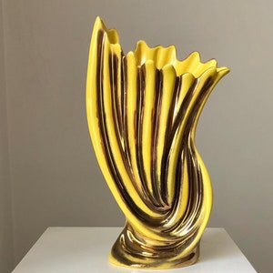 以下が含まれることがあります： 金色のアクセントが付いた黄色の陶器の花瓶。花瓶はユニークな波状のデザインと広い開口部を持っています。