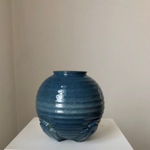 May include: A blue ceramic vase with a round body and a textured surface. The vase has a wide opening and a base with four feet.