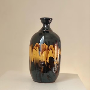 Könnte beinhalten: Eine schwarze Keramikvase mit einer braunen und gelben Marmorierung. Die Vase hat einen runden Körper und einen schmalen Hals.