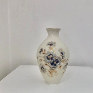 Könnte beinhalten: Eine weiße Keramikvase mit Blumenmuster. Die Vase hat blaue und goldene Blumen mit grünen Blättern.