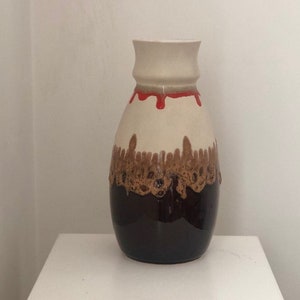 Könnte beinhalten: Eine weiße Keramikvase mit brauner und roter Glasur. Die Vase hat einen runden Körper und einen schmalen Hals.