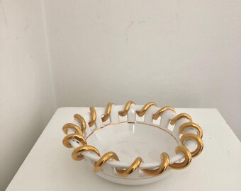 May include: White ceramic bowl with a gold spiral design around the rim. The bowl has a simple, elegant shape with a gold trim. The gold accents provide a striking contrast against the white ceramic.