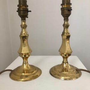 Może przedstawiać: Para złotych lamp stołowych o prostym, eleganckim designie. Lampy mają okrągłą podstawę i wysoki, smukły trzon.