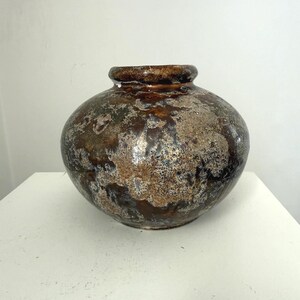 Könnte beinhalten: Eine runde Keramikvase mit breitem Körper und schmalem Hals. Die Vase hat eine gesprenkelte, strukturierte Oberfläche mit Brauntönen, Grau und Beige. Der Rand der Vase ist dunkler braun. Die Vase steht auf einer weißen Oberfläche.