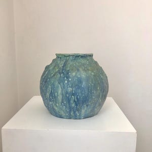 May include: A blue and green ceramic vase with a textured, bubbly surface. The vase has a round shape and a wide opening.
